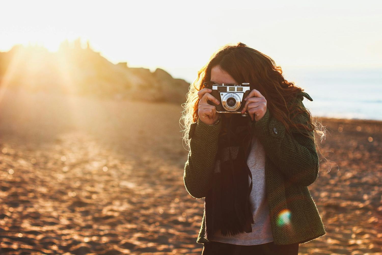 Filmikameran kanssa rannalla Pitkähiuksinen henkilö ottaa kuvaa filmikameralla rannalla.